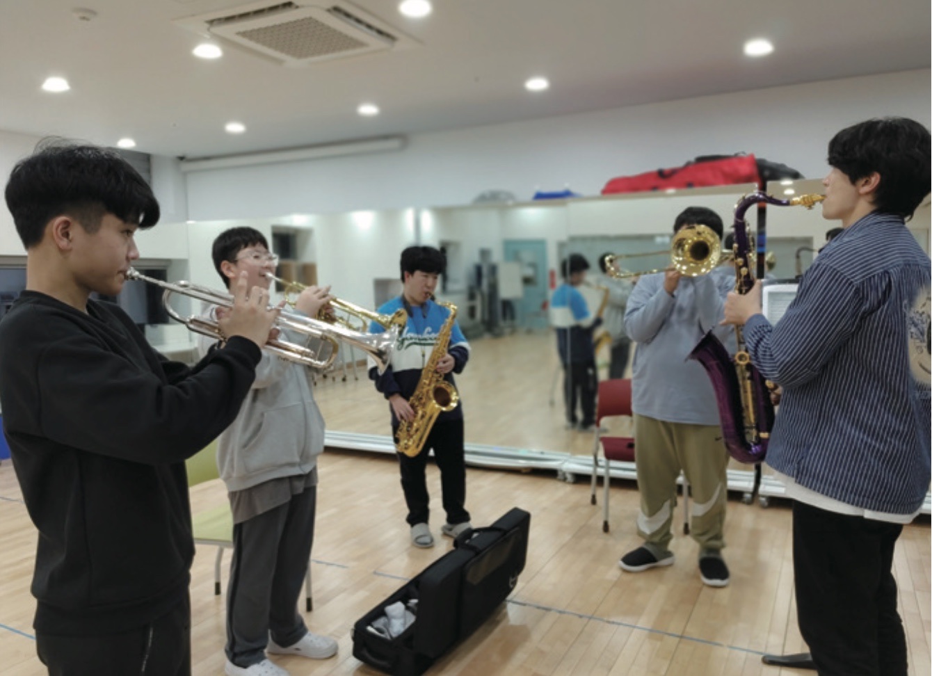 연습실에서 학생들이 트럼펫과 색소폰, 트롬본을 불며 합주하고 있다